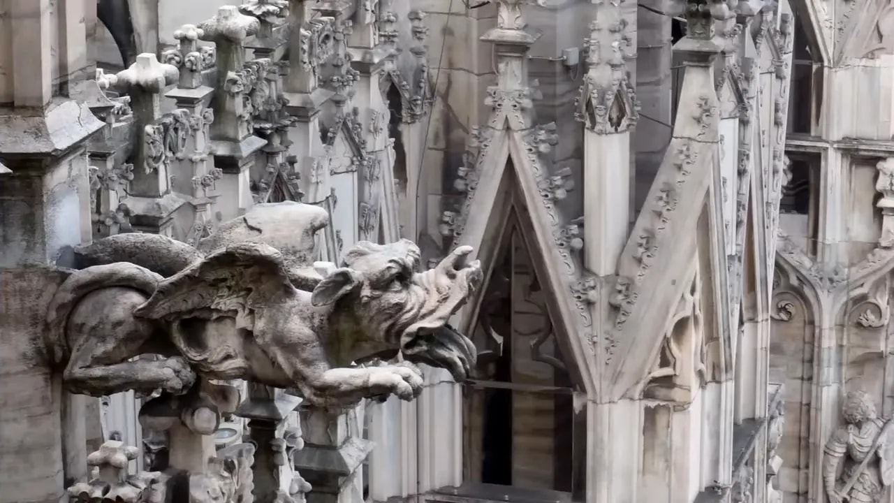 stone gargoyle waterspout with gothic pinnacles and tracery in background