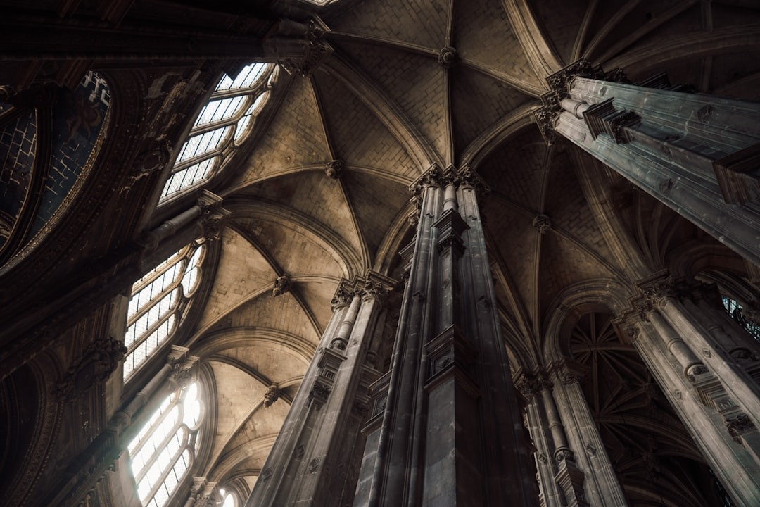 Gothic cathedral interior with tall stone columns and soaring vaulted ceilings, illuminated by natural light streaming through large arched windows. The architecture features intricate details and dramatic shadows.